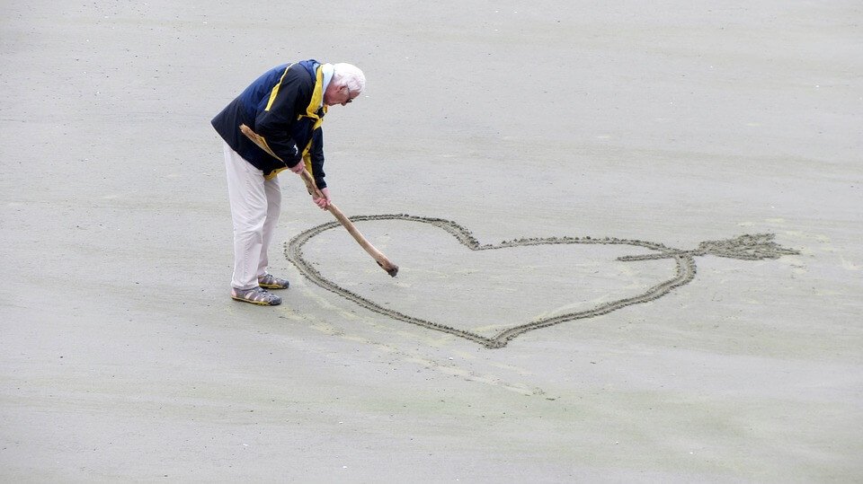 man drawing heart in sand